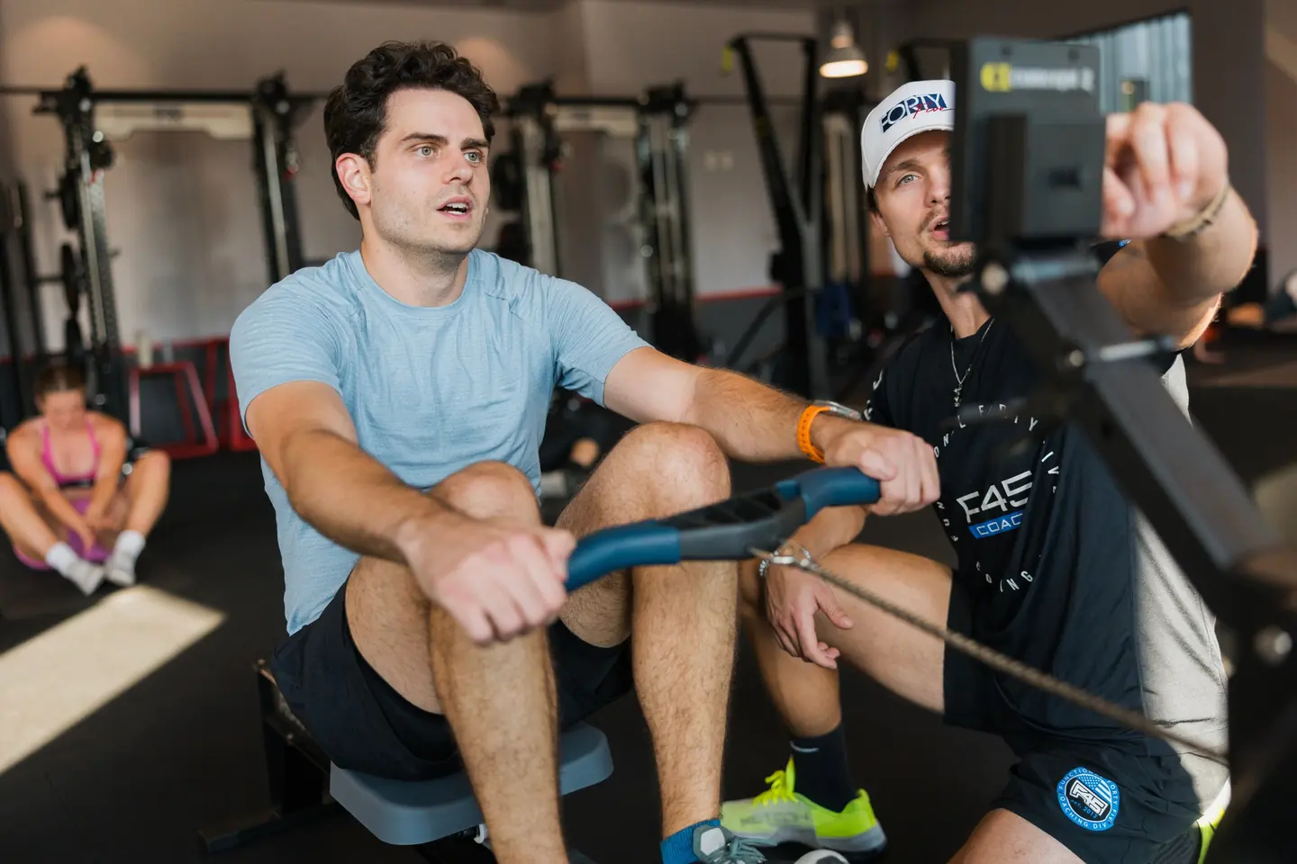 A coach at F45 Training North Weston counting a member through a set on the rowing machine.